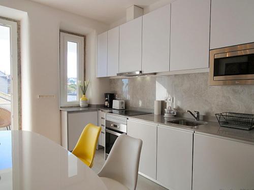 a kitchen with white cabinets and a table and yellow chairs at Panteao - Lissabon Altstadt in Lisbon