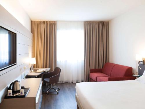 a hotel room with a bed, chair, desk and a television at Novotel Brescia Due in Brescia