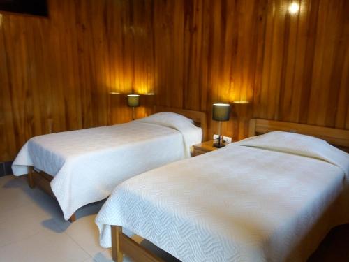 two beds in a room with wooden walls at Hostal La Maison Canadiense in San Ramón