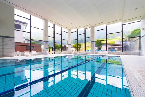 a large swimming pool with blue tiles in a building with windows at Hotel Tangram in Shinano