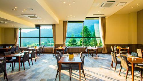een restaurant met tafels en stoelen en grote ramen bij Hotel Tangram in Shinano