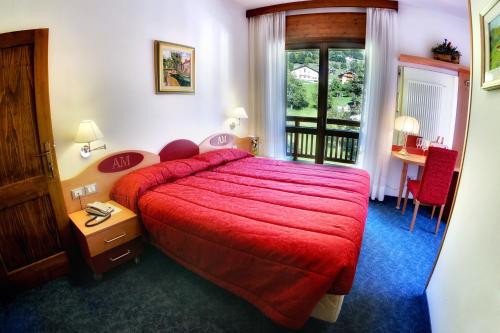 ラッビにあるAlbergo Miramontiの赤いベッドとテーブルが備わるホテルルームです。
