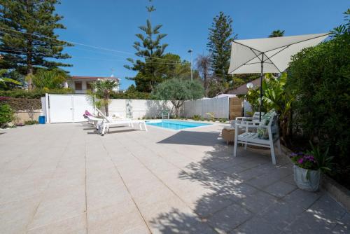 a patio with chairs and an umbrella and a pool at Holiday Fontane Bianche Gabriella in Fontane Bianche