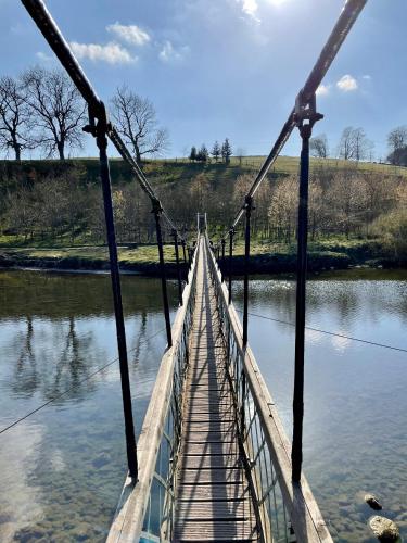 a suspension bridge over a river with water at Apple tree hut, in a private garden in Skipton
