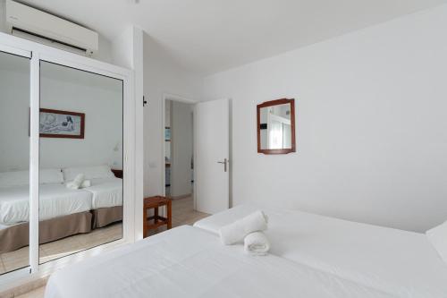 a white bedroom with two beds and a mirror at HomeforGuest Apartamento con terraza y piscina en Corralejo in Corralejo