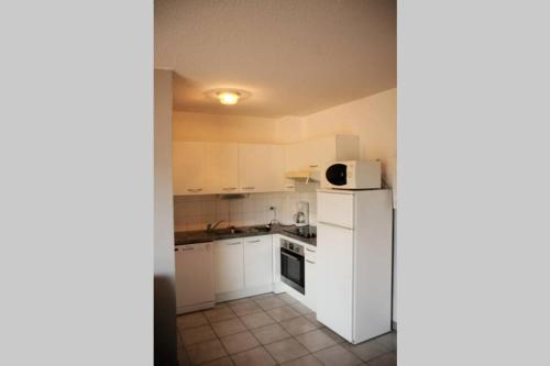 une petite cuisine avec des armoires blanches et un micro-ondes dans l'établissement T3 familial avec accès direct à la plage., à Banyuls-sur-Mer