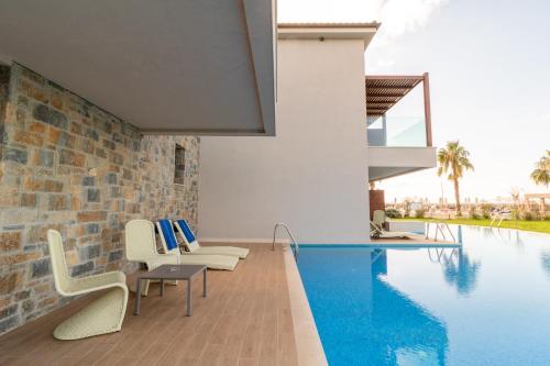 a swimming pool with white chairs and a brick wall at Almyros Beach in Acharavi