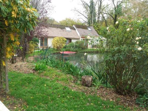 uma casa com um lago em frente a um quintal em La petite campagne em Blaru