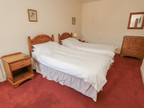 a bedroom with a bed with white sheets and a night stand at Manor Cottage in Wooler