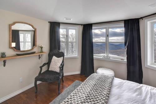 a bedroom with a bed and a chair and windows at Ski-in/Car-out, HOT TUB with Amazing sunset view in Saint-Faustin