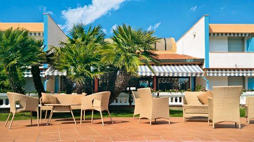 un grupo de sillas y mesas en un patio con palmeras en Hotel Riva Etrusca, en Marina di Bibbona