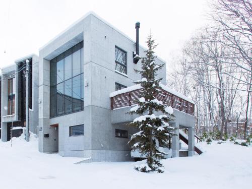 a building with a snow covered tree in front of it at Kita Kitsune Chalet in Kutchan
