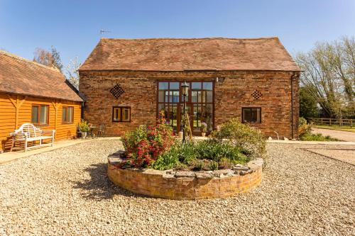 een bakstenen huis met een groot raam en bloemen ervoor bij Bridge Farm Holiday Cottages in Cow Honeybourne