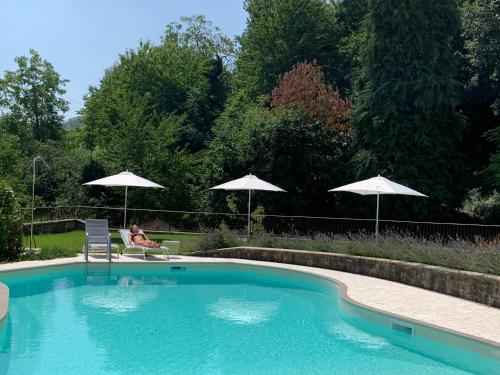 a woman sitting in a chair next to a pool with umbrellas at Borgo La Morra in Pavullo nel Frignano