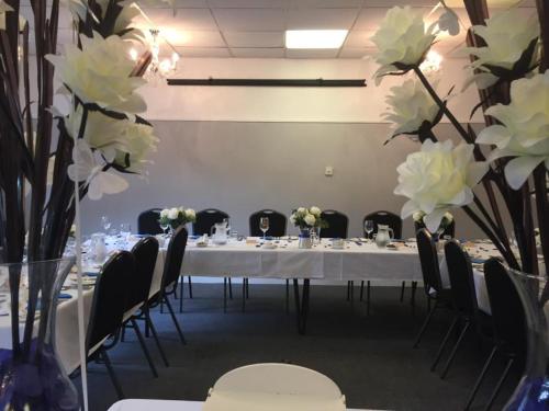 a long table with chairs and white flowers in a room at The Quorn Lodge Hotel in Melton Mowbray