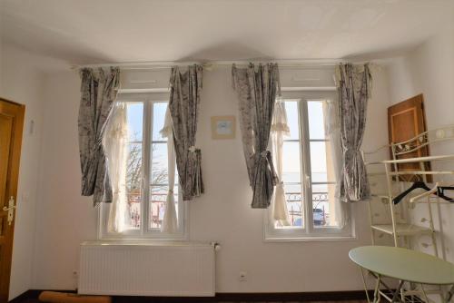 Zimmer mit 2 Fenstern, Vorhängen und einem Tisch in der Unterkunft Les Mouettes Blessées in Le Crotoy