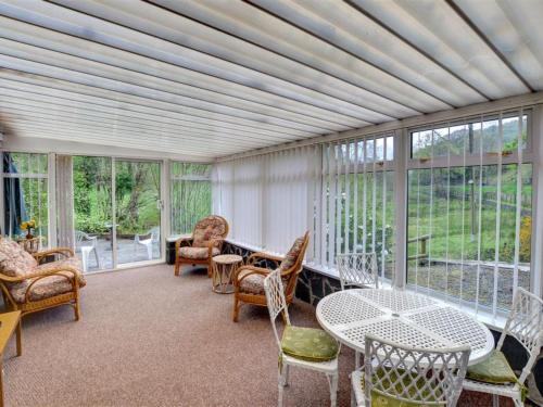 a screened in porch with chairs and tables and windows at Holiday Home Pantperthog by Interhome in Esgair-geiliog