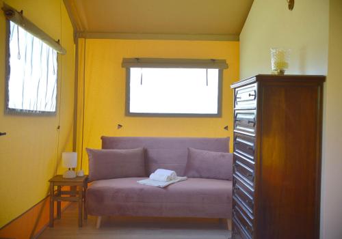 a purple couch in a yellow room with a window at Glamping Tenuta San Pierino Agriturismo in Rosignano Marittimo