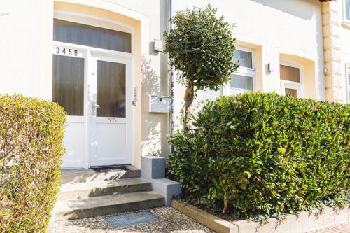 a white front door of a white house with bushes at Skerra Apartments "am Fitness-Studio" in Fehmarn