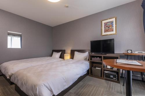 a hotel room with two beds and a desk with a television at Tofukuji Riverside in Kyoto