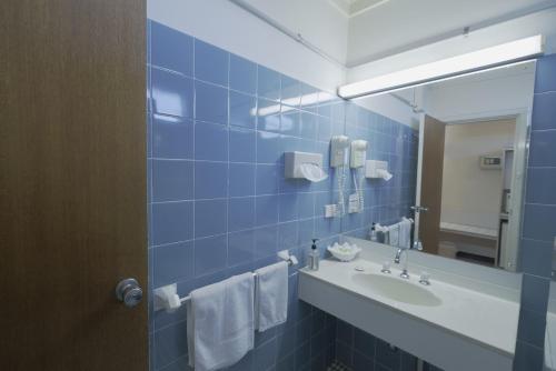 bagno piastrellato blu con lavandino e specchio di Olympia Motel a Queanbeyan