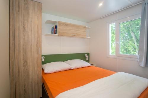 a bedroom with an orange and white bed with a window at CHERRY Premium JADE Mobile homes Zelena Laguna in Poreč