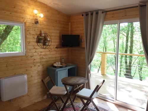 Zimmer mit einem Tisch, Stühlen und einem TV in der Unterkunft Les Cabanes du Lac - SPA - Petit Déjeuné - Cabane du frêne & Cabane du chêne Premium in Sévignac-Thèze