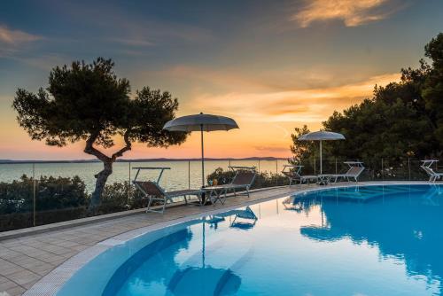a swimming pool with chairs and umbrellas and the ocean at Hotel Pinija in Petrcane