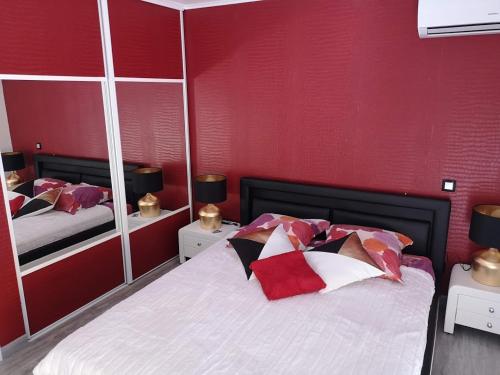 1 dormitorio con 1 cama con paredes rojas y espejos en Chambre La Palmeraie village naturiste, en Cap d'Agde