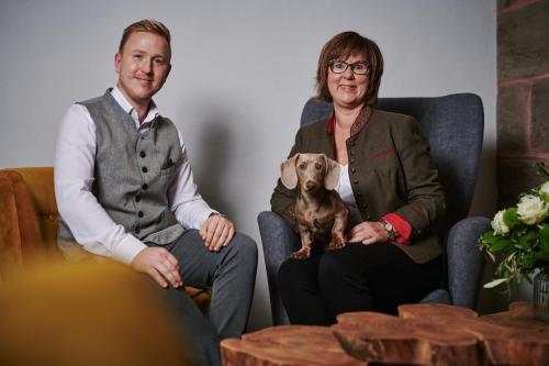 a man and woman sitting in chairs with a dog at DER SCHWAN Hotel & Restaurant in Schwanstetten
