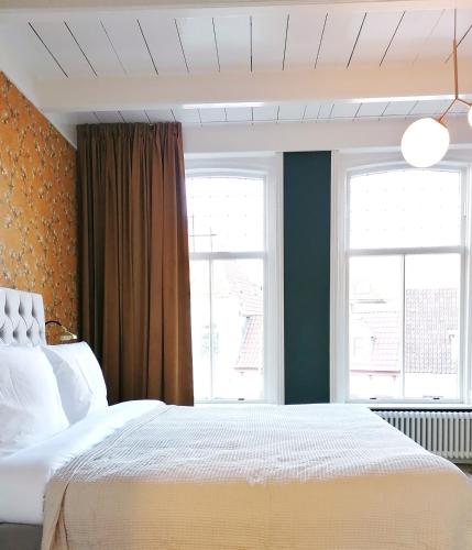 um quarto com uma cama branca e 2 janelas em B&B De Stadssingel em Steenwijk