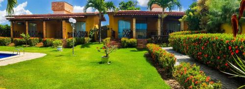 a house with a green yard with flowers in front of it at Pousada Aconchego in Pitimbu