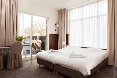 - une chambre avec un grand lit et une table avec une personne assise dans une chaise dans l'établissement Hotel Stad en Land, à Alkmaar