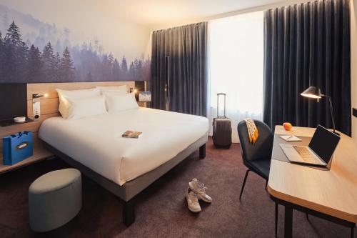 a hotel room with a bed and a desk with a laptop at Novotel Annemasse Centre - Porte de Genève in Annemasse
