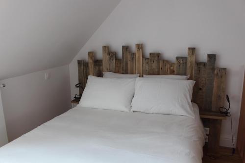 uma cama branca com uma cabeceira em madeira e almofadas brancas em Maison de charme en plein centre ville em Montreuil-sur-Mer