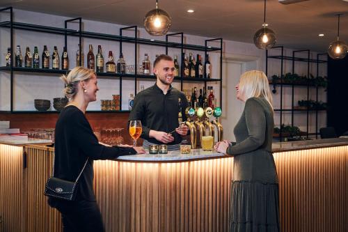 two women and a man standing at a bar with wine glasses at Hotel Oasia Aarhus City in Aarhus