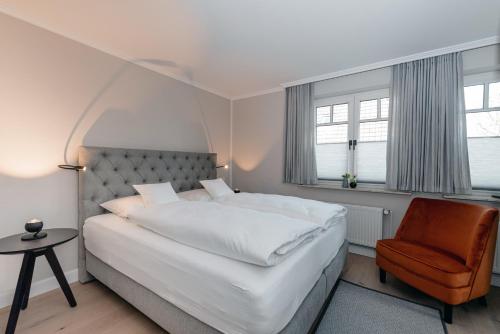 ein Schlafzimmer mit einem großen weißen Bett und einem Stuhl in der Unterkunft Jaumann's Südwind Sylt in Westerland