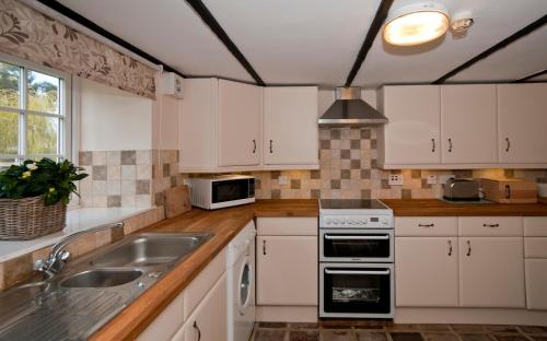 a kitchen with white cabinets and a sink at Tros Yr Afon Holiday Cottages and Manor House in Beaumaris