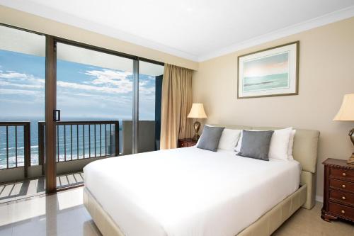1 dormitorio con cama blanca y balcón en BreakFree Longbeach Resort, en Gold Coast