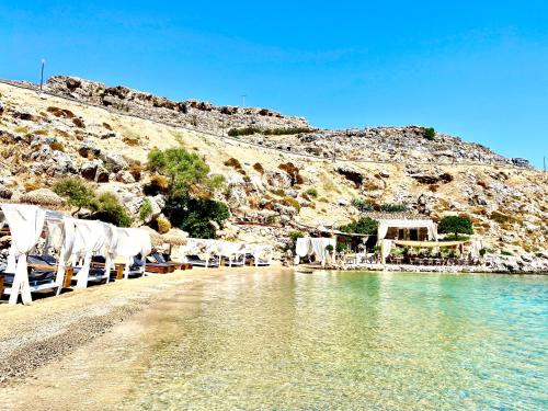 a beach with white chairs and the water at Lindos Serenity Suites in Líndos