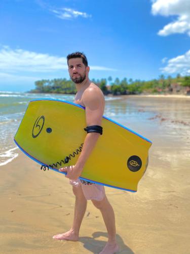 a man standing on the beach holding a yellow surfboard at Apto Praia da Taíba Vista Mar in Taíba