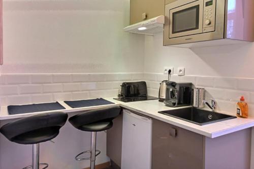a kitchen with two stools and a sink and a microwave at Les Appartements Fénelon in Le Cateau