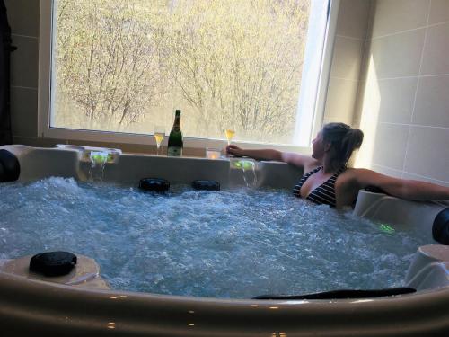Hôtel Le Cassini في Le Freney-dʼOisans: امرأة تجلس في حوض استحمام ساخن مع زجاجة من النبيذ