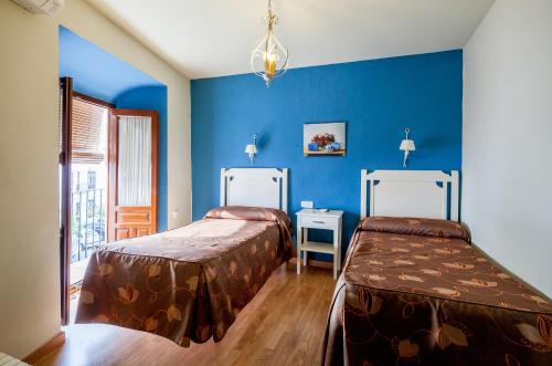 2 camas en una habitación con paredes azules en Hostal El Caballo Blanco, en Osuna
