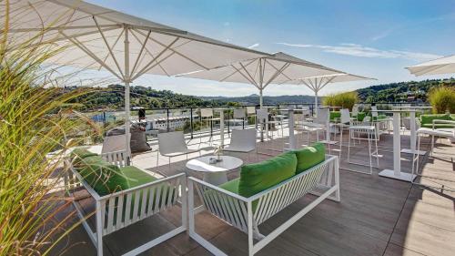 un patio con sillas blancas, mesas y sombrillas en Hotel am Remspark en Schwäbisch Gmünd