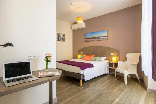 a hotel room with a bed and a desk with a laptop at CIT'HOTEL Le Commerce in Saujon