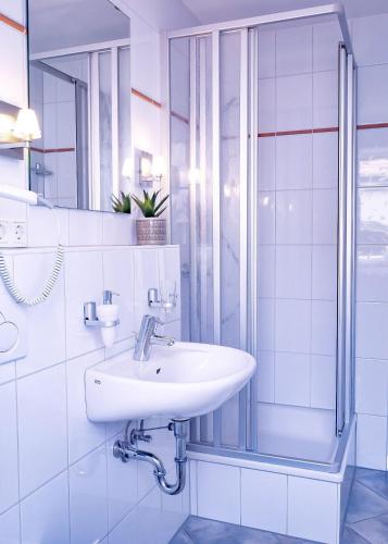 La salle de bains blanche est pourvue d'un lavabo et d'une douche. dans l'établissement Flippi-s-Hues-NORD, à Westerland