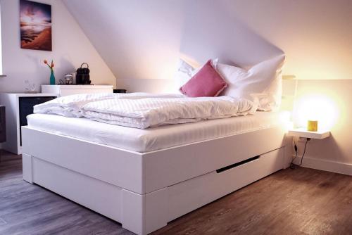 a white bed with white sheets and pink pillows at Flippi-s-Hues-SUeD in Westerland (Sylt)