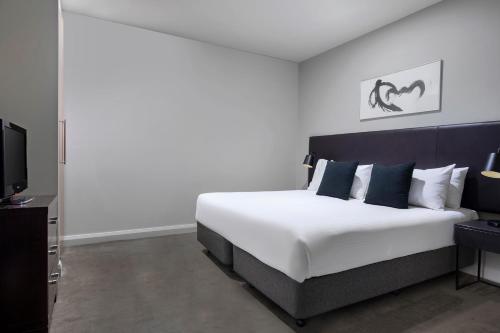 a bedroom with a large white bed and a tv at Mantra Hindmarsh Square in Adelaide