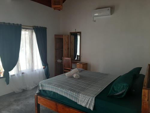 a bedroom with a bed with a green blanket and a window at Kambuna Bungalow in Krui